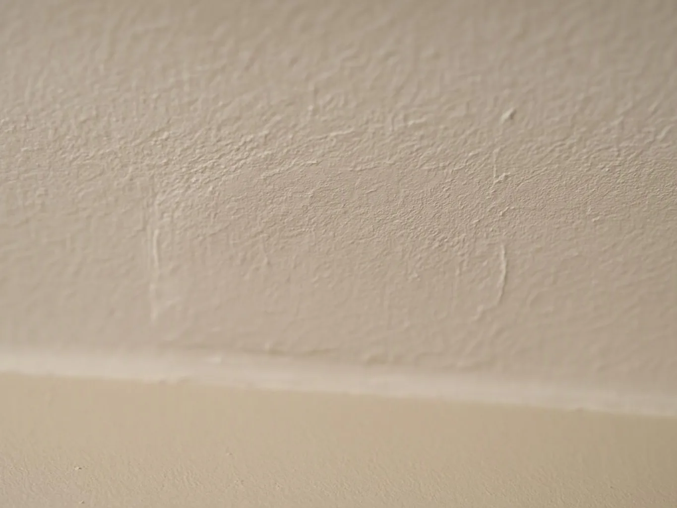 A close-up of a beige textured wall with a white trim line near the bottom