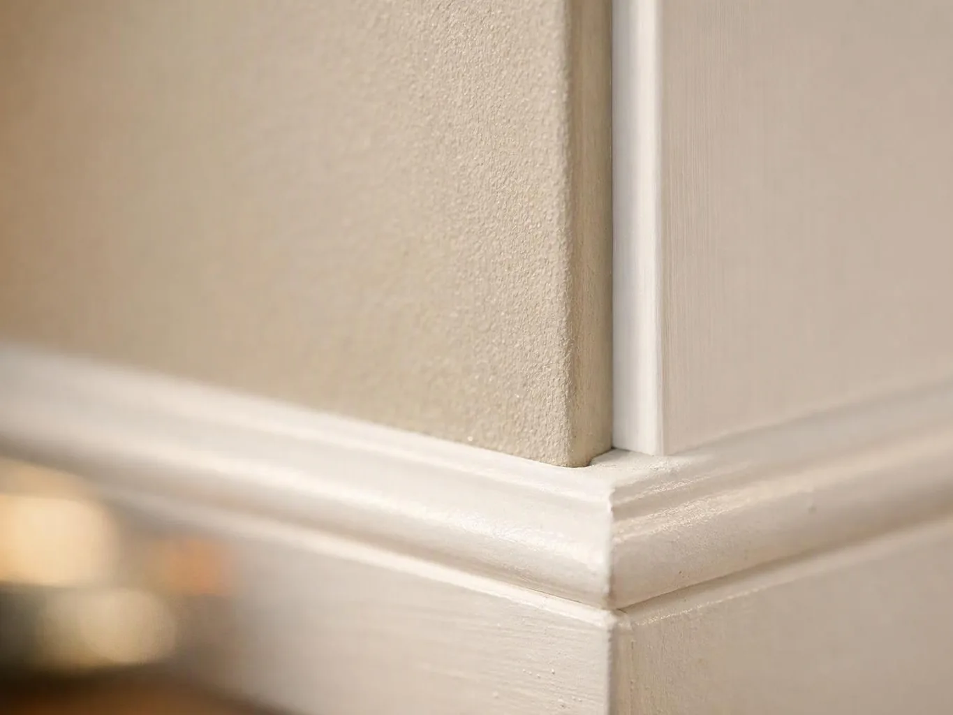 Close-up of a beige wall corner with white trim and molding in soft indoor light
