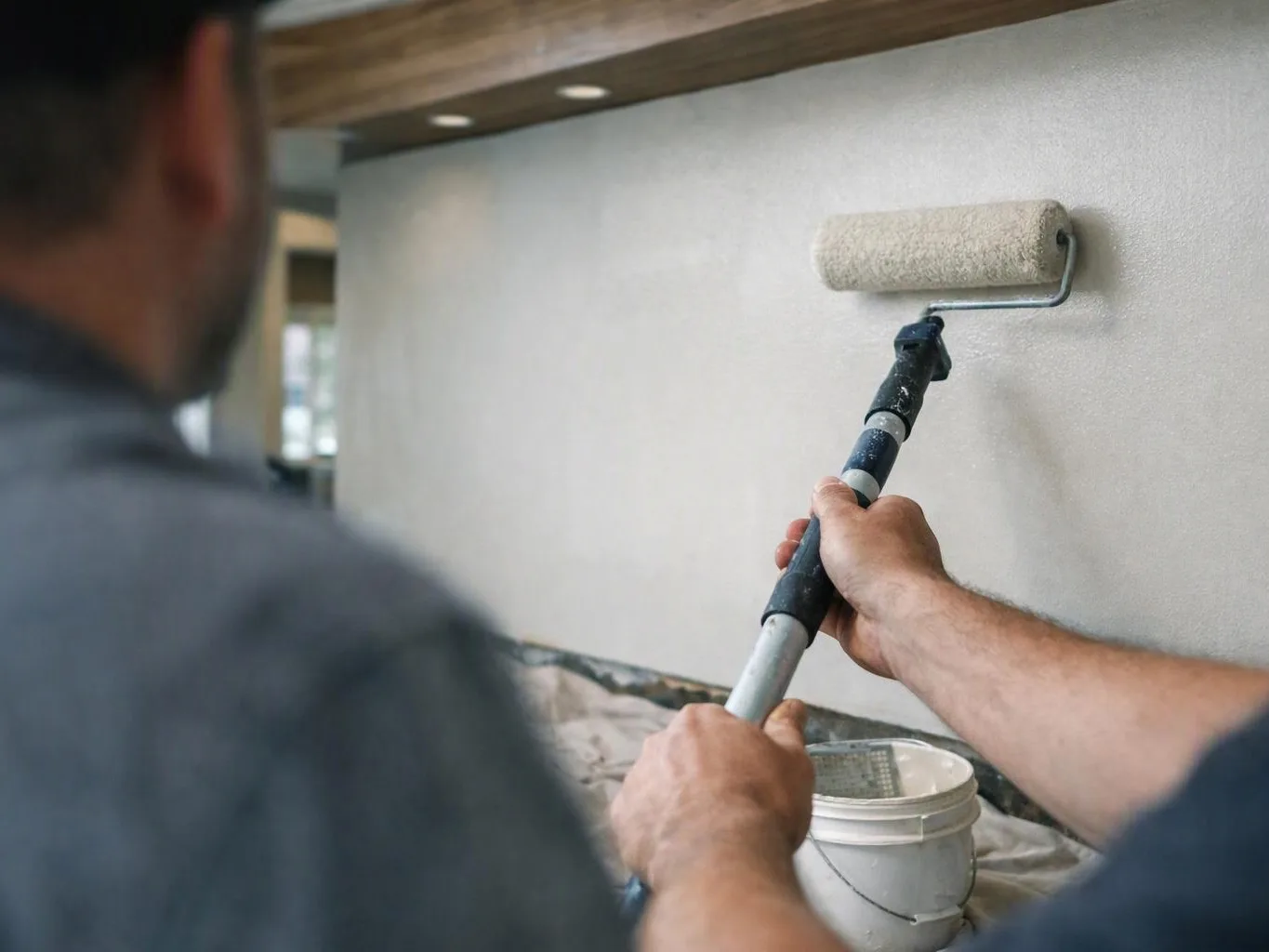 Two workers paint a wall with a roller in a room under construction